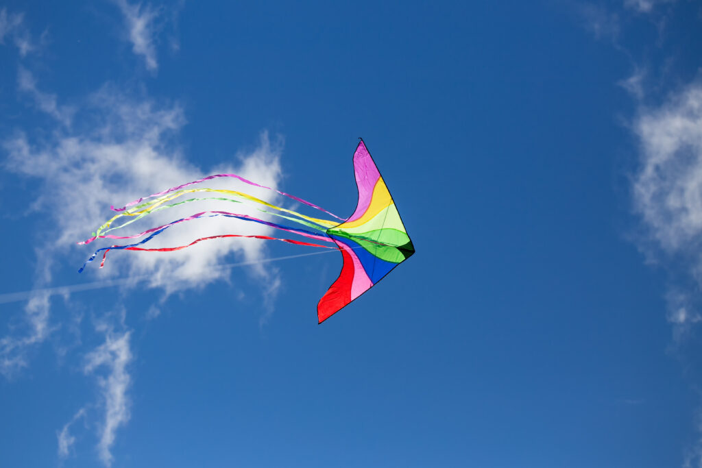 A colorful triangle kite flies under blue sky. sunny autumn.