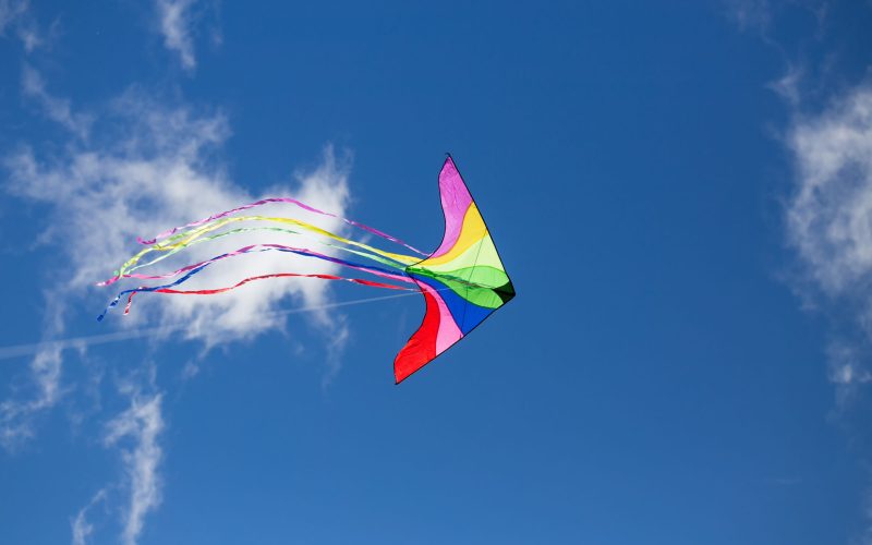 A colorful triangle kite flies under blue sky. sunny autumn.